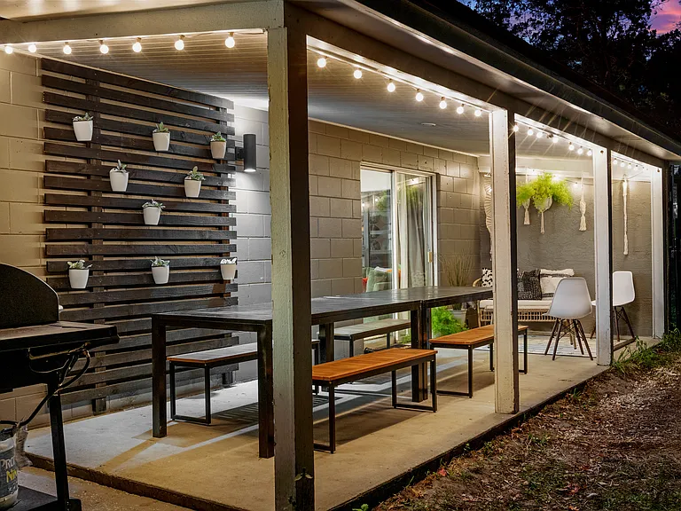 Covered porch off living room with outdoor dining area, seats ten, with string lights and large dual fuel (charcoal and propane) grill - night time