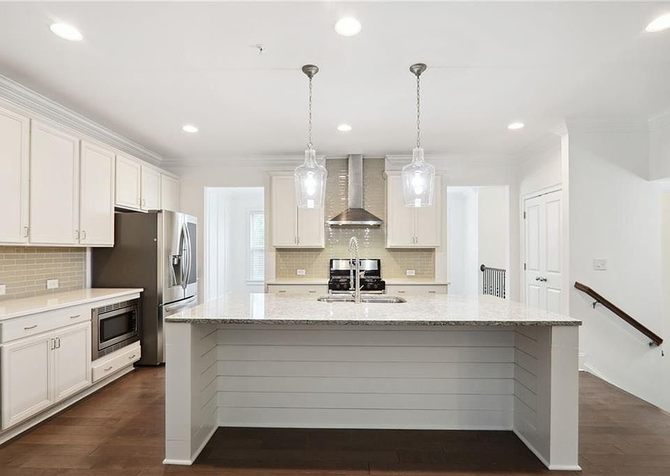 Kitchen - Kitchen featuring appliances with stainless steel finishes, an island with sink, wall chimney exhaust hood, white cabinets, and dark hardwood / wood-style flooring