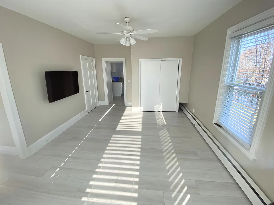 A spacious living area that flows naturally toward the kitchen, featuring a ceiling fan, a side wall window for added natural light, and convenient access near the secondary entry.