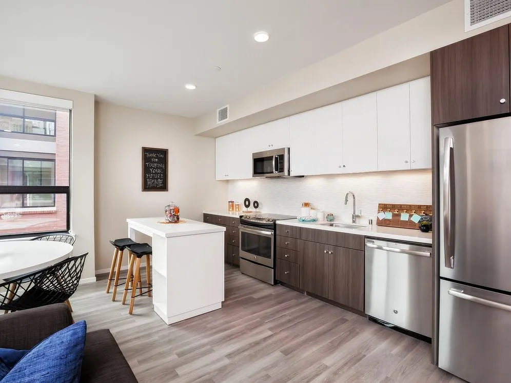 Open concept kitchen with stainless steel appliances, white and brown cabinetry, quartz stone countertop, ceramic tile backsplash, island table and hard surface flooring - Avalon Dogpatch