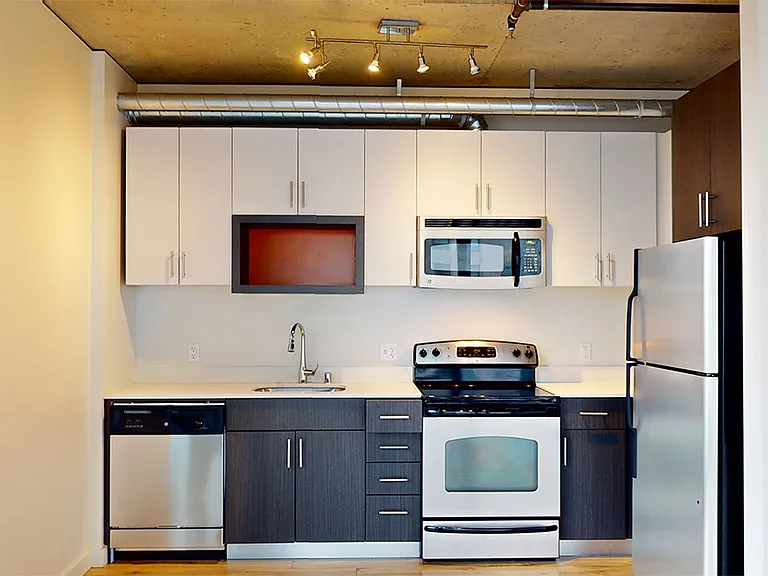 Apartment kitchen with stainless steel appliances, quartz countertops and wood-style flooring.