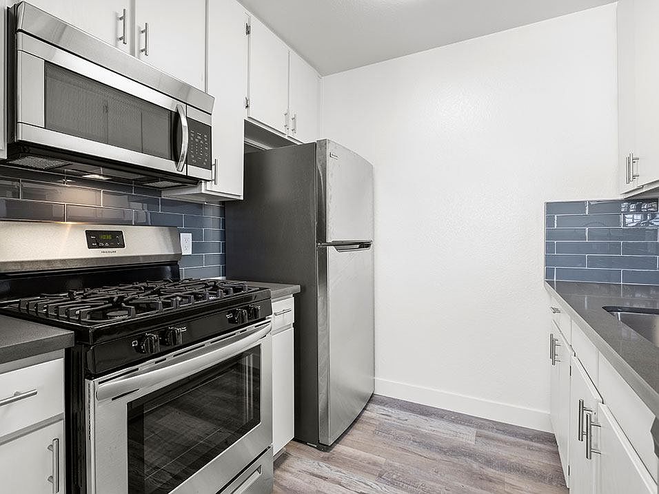 Blue tiled kitchen with stainless steel oven, microwave, and fridge.