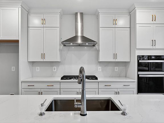 A modern, white kitchen with stainless steel appliances, including a range hood and a double oven, a