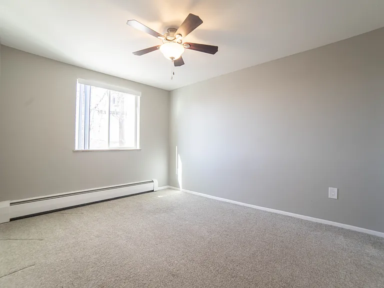 Bright and inviting empty room with neutral walls, soft carpet, and a modern ceiling fan, ready to be personalized.