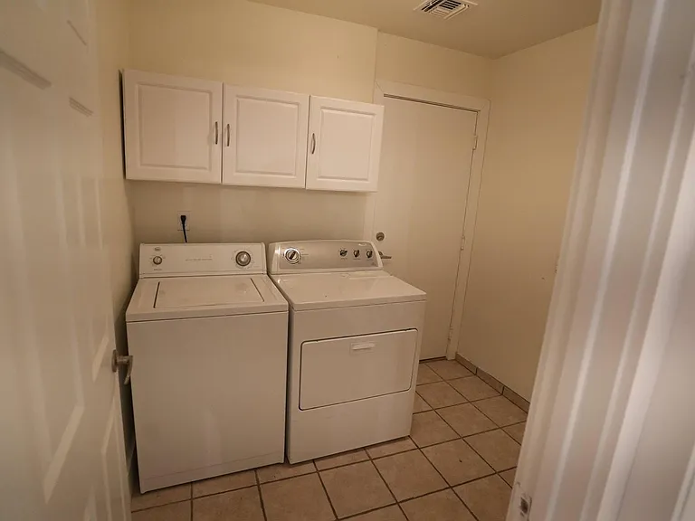 Dedicated laundry room with full-size washer and dryer plus wall-mounted cabinets for convenient storage.