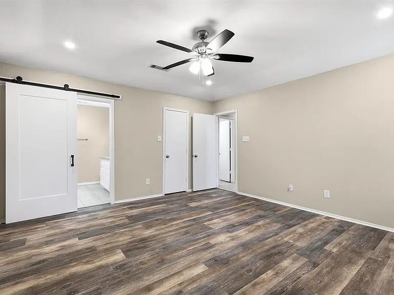 Unfurnished bedroom featuring a barn door, wood finished floors, connected bathroom, ceiling fan, and recessed lighting