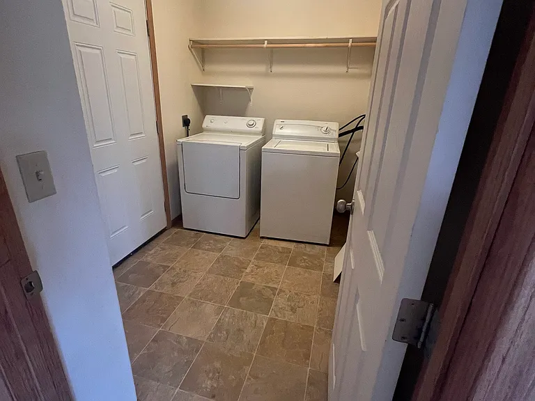 Full laundry / storage room with hook ups and wall shelving for storage.