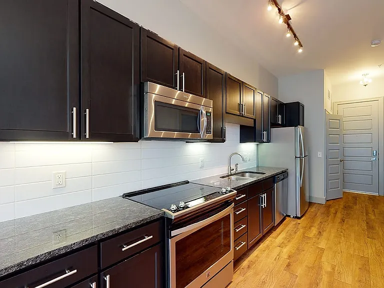 Apartment kitchen with stainless steel appliances, granite countertops and wood-style flooring.