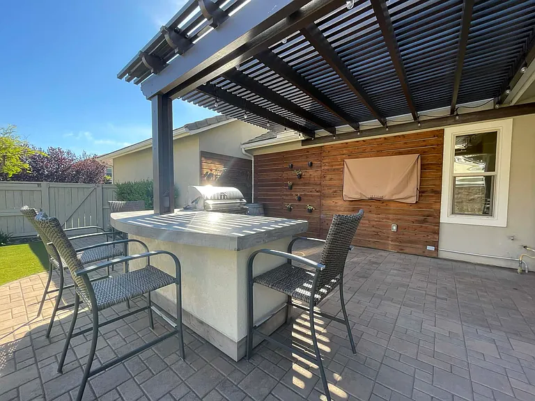 Pergola covered grill and bar area with bar stools, grill and refrigator.