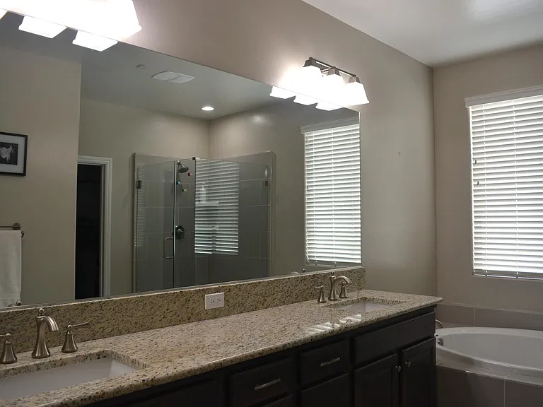 Primary bathroom showing granite countertops, double sink, bathtub, frameless shower enclosure