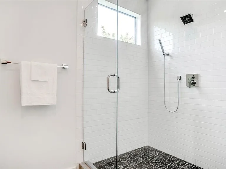 Glass-enclosed shower with white subway tile walls, dark pebble-style flooring, a fixed rain shower head, and a handheld shower spray