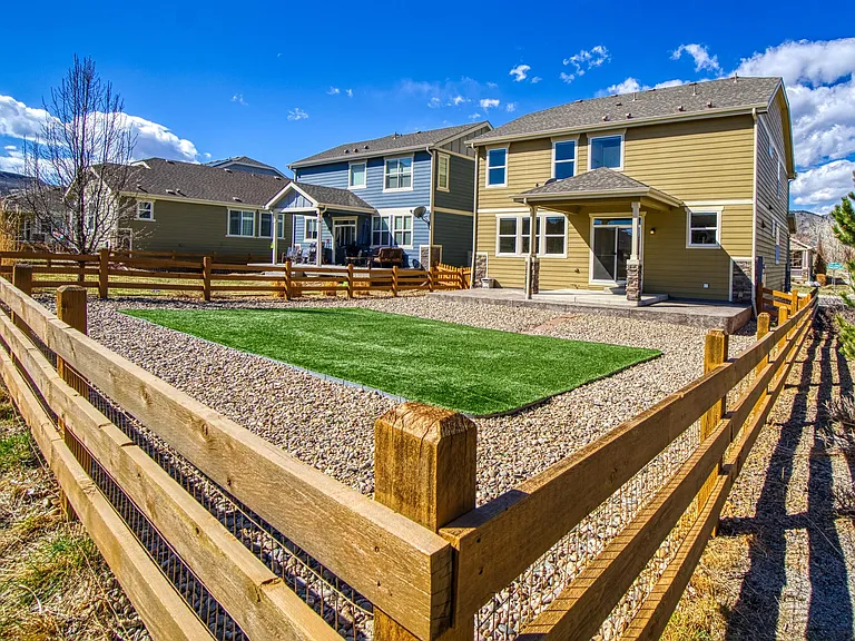 No-maintenance fenced-in backyard with realistic artificial grass, river rock, covered patio, natural gas line for grill, and views of North Table Mountain.
