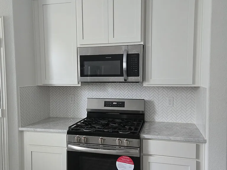 Functional kitchen nook with white shaker cabinetry, herringbone tile backsplash, and a gas range with over-the-range microwa