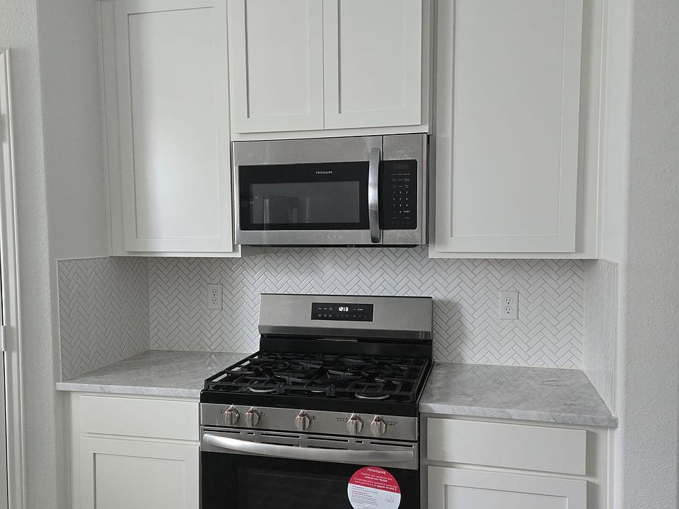 Functional kitchen nook with white shaker cabinetry, herringbone tile backsplash, and a gas range with over-the-range microwa