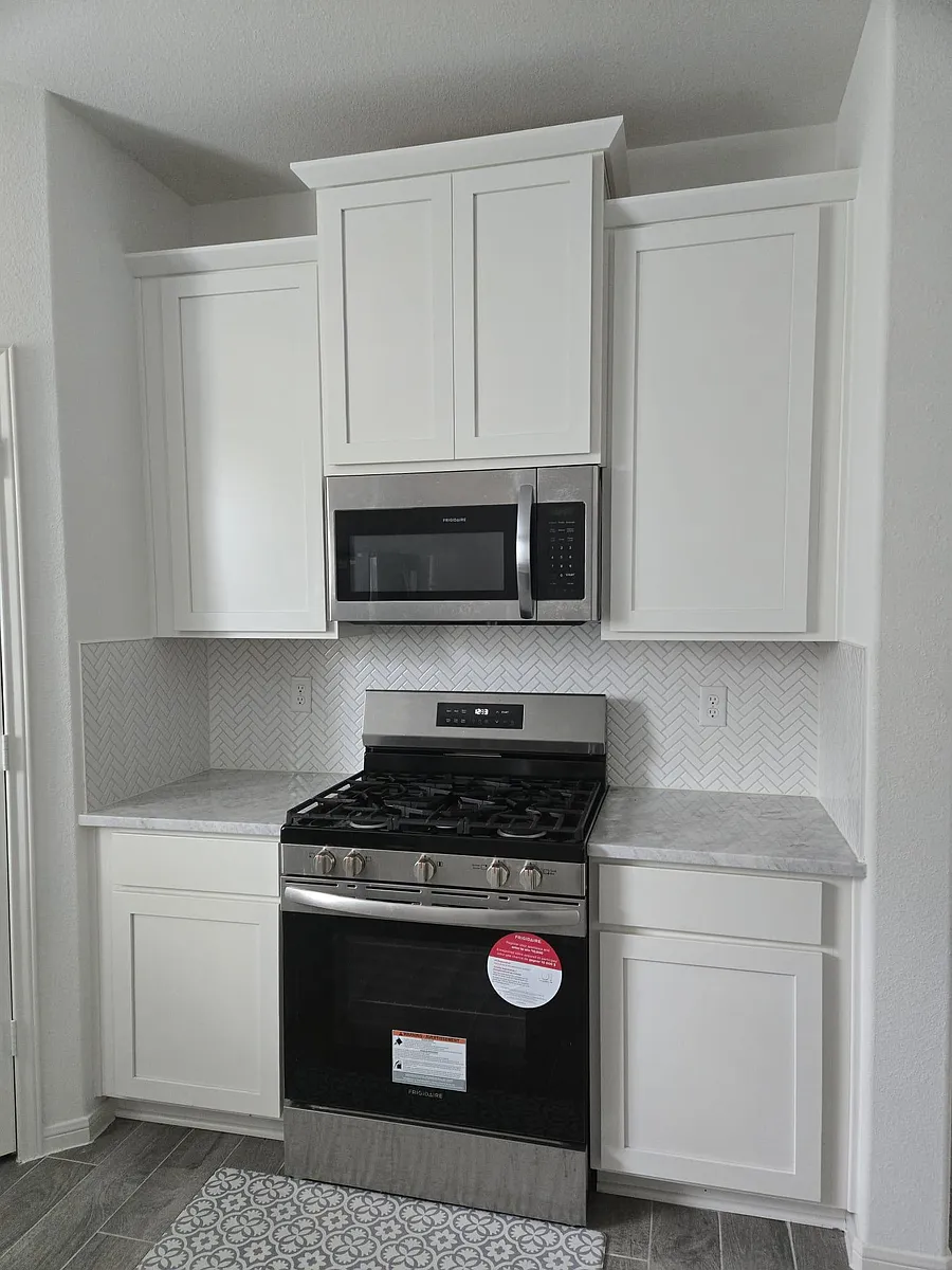 Functional kitchen nook with white shaker cabinetry, herringbone tile backsplash, and a gas range with over-the-range microwa - Sterling Oak Dr