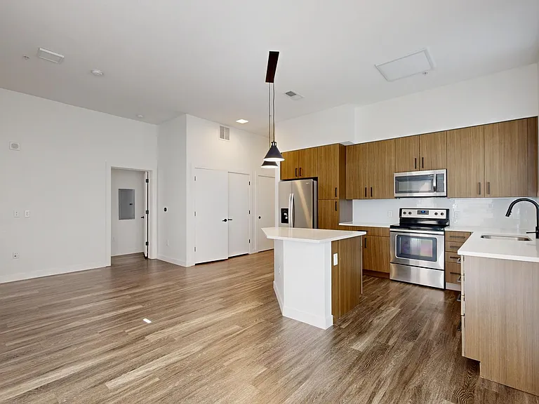 Apartment kitchen with stainless steel appliances, dining and living room with wood-style flooring.