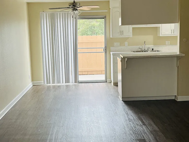 Kitchen, dining area with ceiling fan and living room with sliding glass doors to patio at Plaza Verde Apartments in Escondido, California.