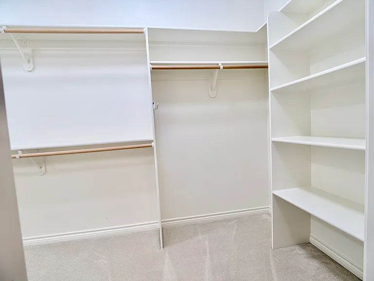 Expansive C-shaped walk-in closet, appointed with abundant shelving and generous hanging space.