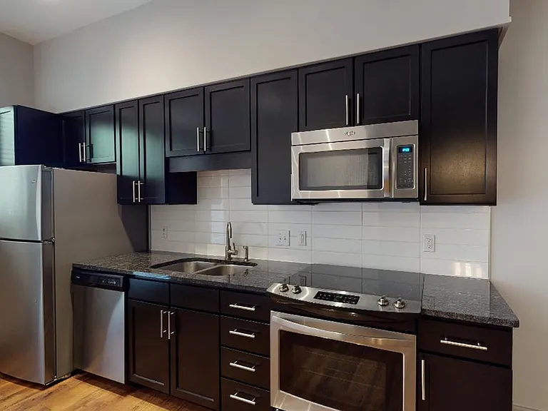 Apartment kitchen with stainless steel appliances, granite countertops and wood-style flooring.