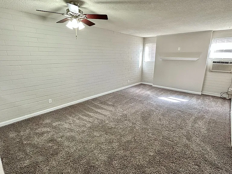 Bright, spacious living room with fresh carpet, elegant ceiling fan, and natural light through large windows.