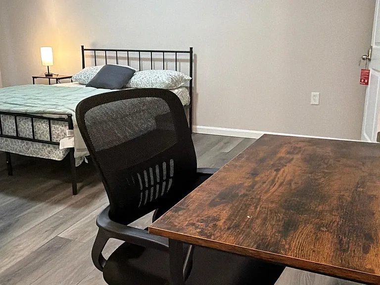 Furnished bedroom with a full bed, bedside lighting, and a dedicated work desk for studying or remote work.