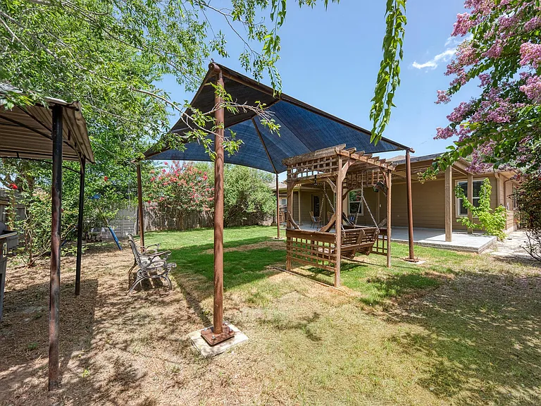 The yard includes a covered swing bench, stationary bench, covered BBQ grill, swing set, and storage shed.