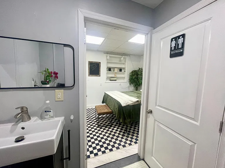 Clean, well-lit bathroom area with a pedestal sink and mirror, plus easy access to an adjacent furnished room.