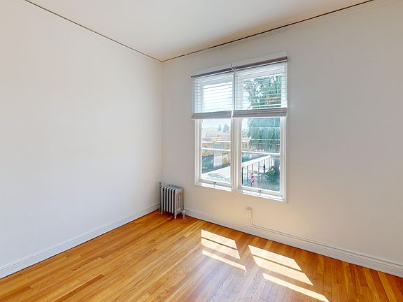 Bright, empty room with hardwood floors, large window with blinds, and a vintage radiator, showcasing a minimalist design