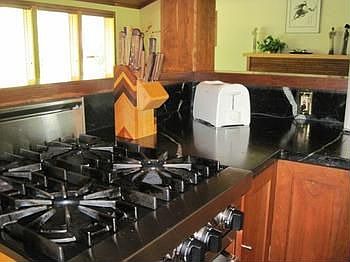 VIKING range with gleaming natural soapstone counter tops. Range has 6 burners and a grill.(some not visible in picture). 2 ovens one conventional and one is convection.  Above the stove is a viking hood with fan, and warmers. 