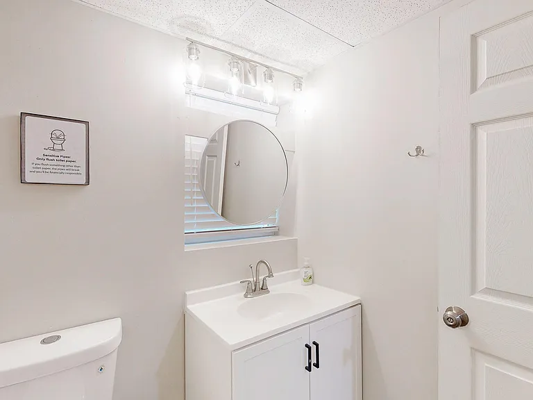 Clean bathroom vanity area with round mirror, ample counter space, and overhead lighting for everyday routines.
