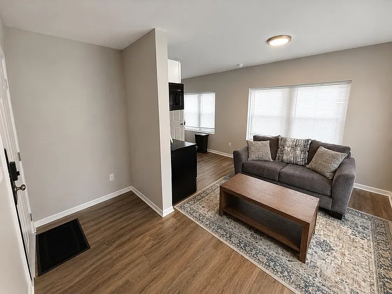 Comfortable living area with wood-look floors, a spacious seating zone, and large windows with blinds for natural light.