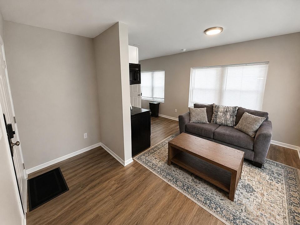 Comfortable living area with wood-look floors, a spacious seating zone, and large windows with blinds for natural light.