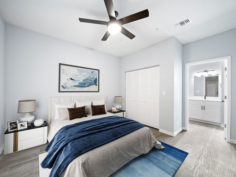 Model home bedroom fully furnished with a closet and bathroom mirror and cabinets in view.