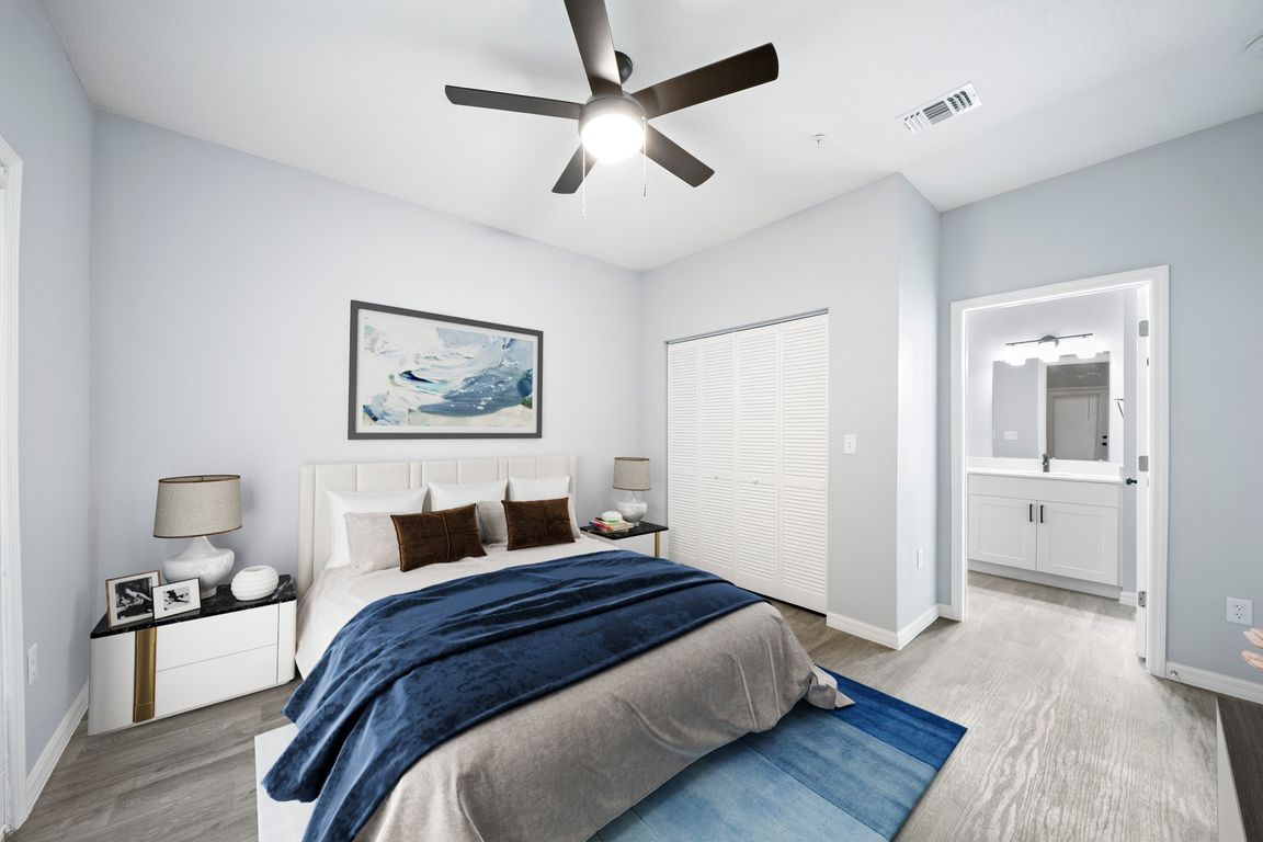 Model home bedroom fully furnished with a closet and bathroom mirror and cabinets in view.