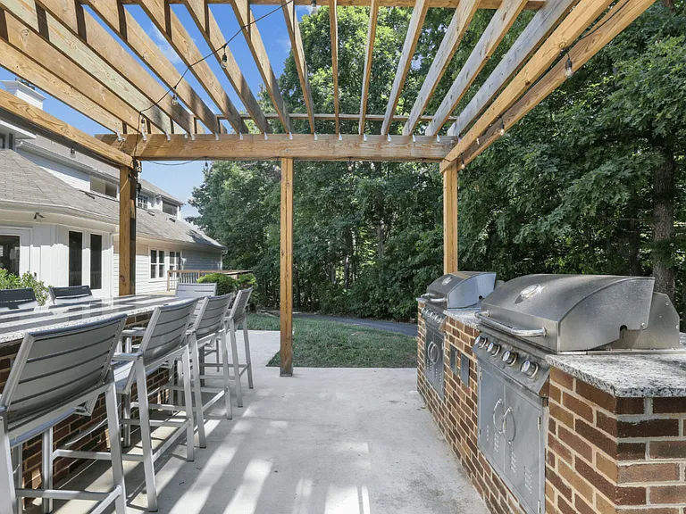 A wooden pergola with a large table and chairs by two BBQ grills at The Crossings at Russett in Laurel, MD