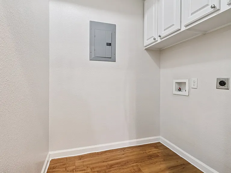 Charming utility room featuring elegant white cabinetry and warm wood-style flooring, perfect for laundry or extra storage. Charming utility room featuring elegant white cabinetry and warm wood-style flooring, perfect for laundry or extra storage.