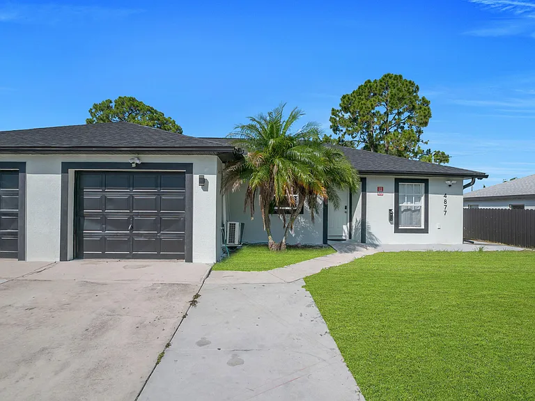 Single-story home with a wide driveway, attached garage, and a grassy front yard with mature palm landscaping.