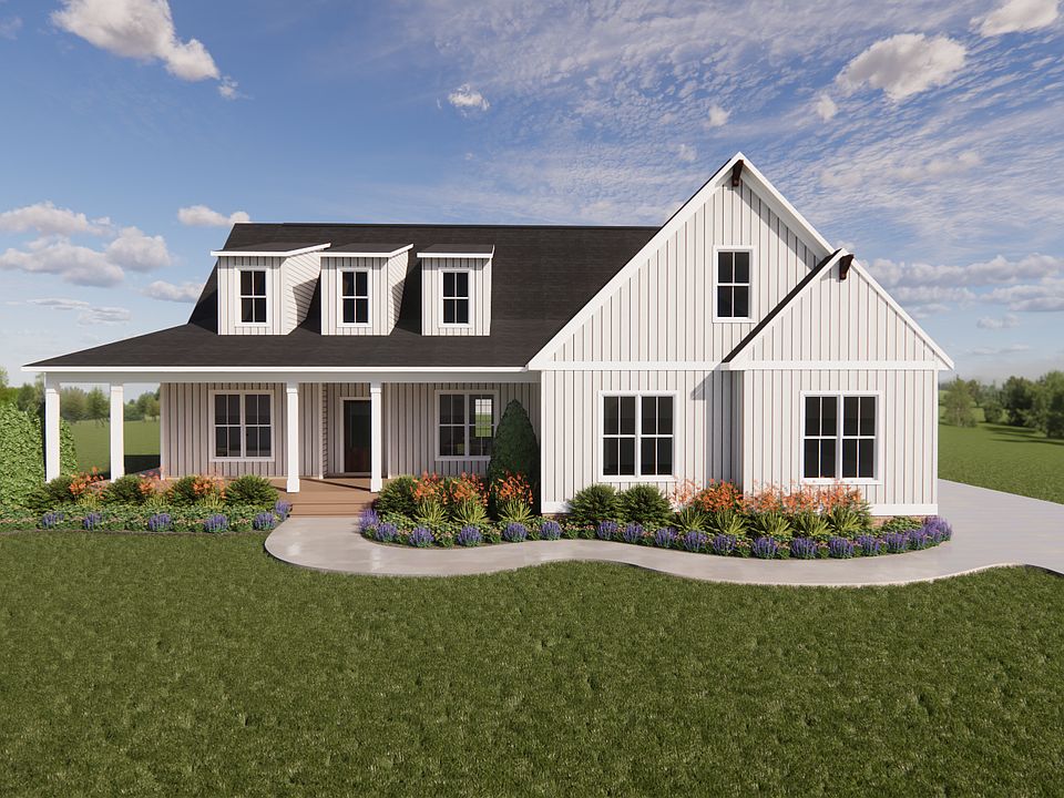 White farmhouse with black roof in Shirley Commons, front porch, dormers, and colorful landscaping o