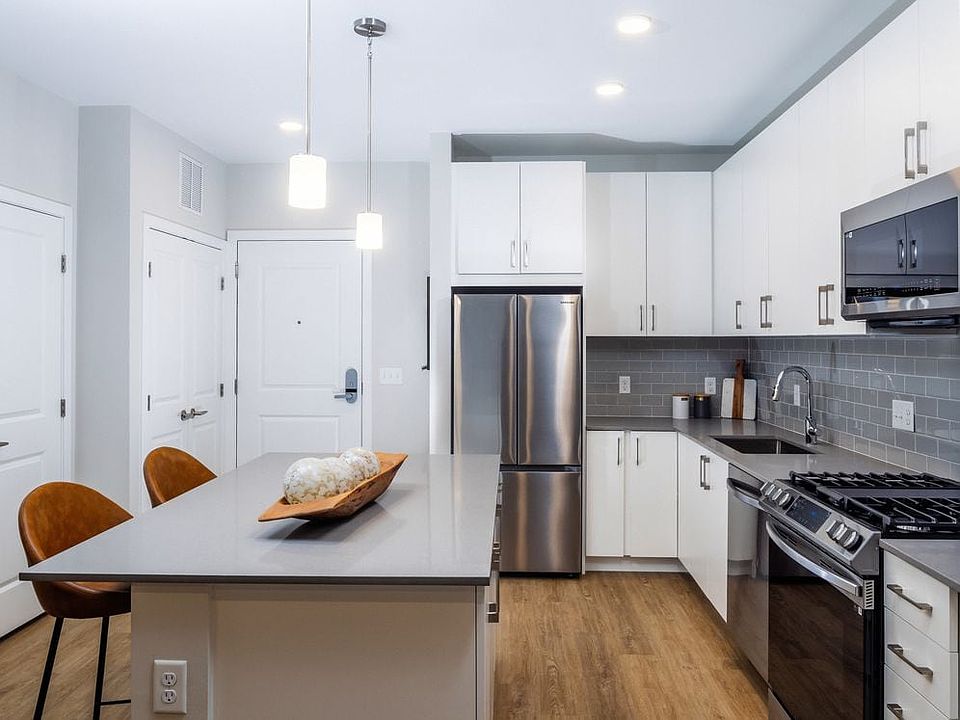 Modern kitchen with white cabinetry, grey tile backsplash, grey quartz countertops, and stainless steel appliances
