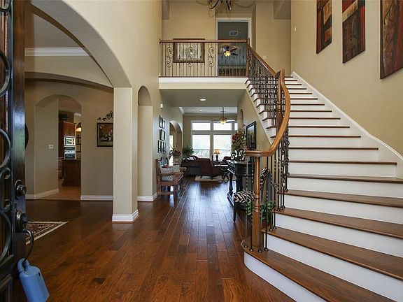 Foyer With Dynamic Curved Staircase With Wood Steps & Arched Doorways Into Formal Dining Room.
