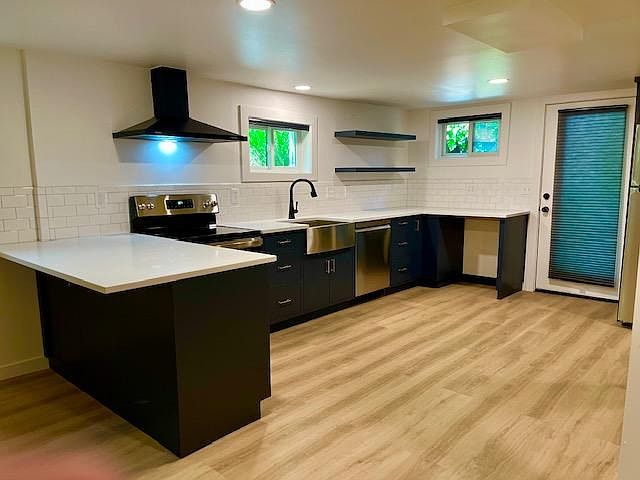 Brand new everything, custom cabinets painted in a deep navy/grey, solid white quartz countertop, white subway tile backsplash, dishwasher, stove, stainless oversized apron sink floating shelves, and entrance door. To the left of the entrance door is a s