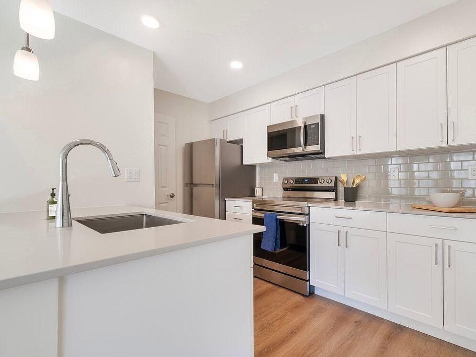 Renovated Package II kitchen with stainless steel appliances, beige quartz countertops, white cabinetry, light grey tile backsplash, and hard surface flooring