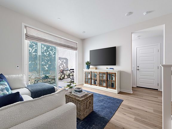 A cozy and modern living room with a large window, a gray sofa, a wooden cabinet, and a blue rug on