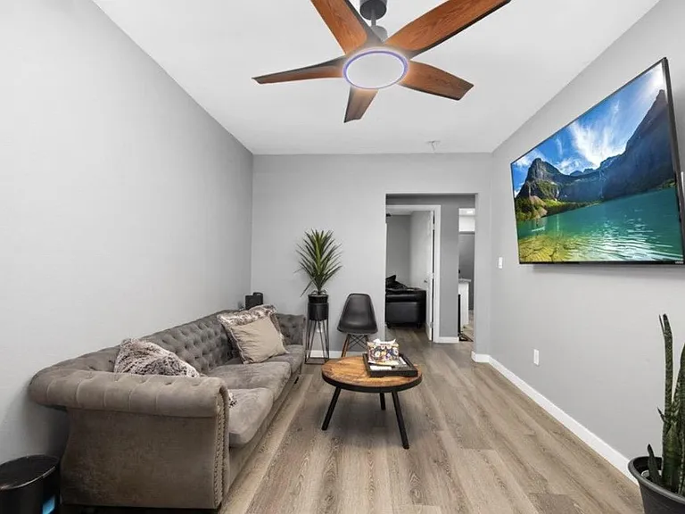 Comfortable living area with wood-look flooring, ceiling fan, wall-mounted TV, and seating for relaxing or entertaining.