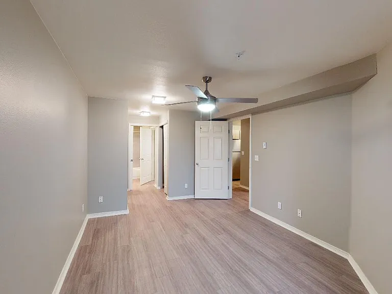 Spacious apartment bedroom with attached bathroom and wood-style flooring.