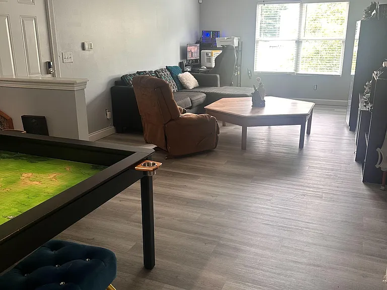 Spacious living room with plank-style flooring, ceiling fan, and a large window for natural light and comfortable seating.