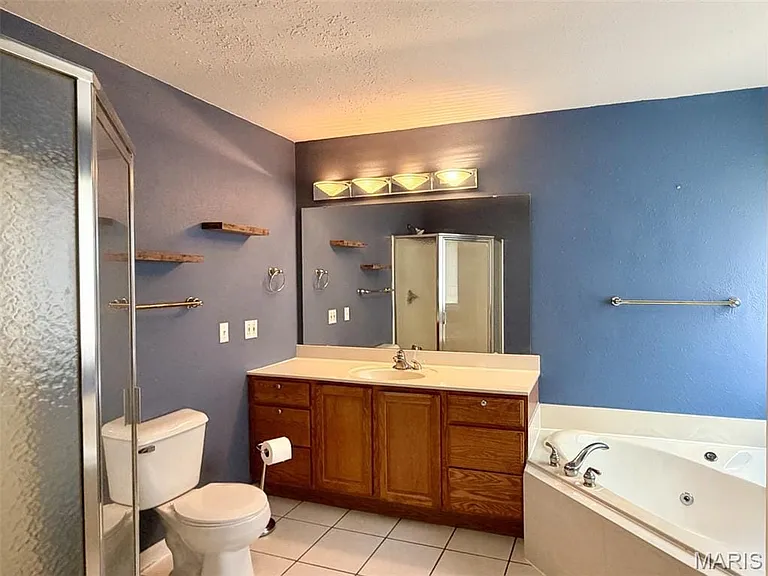 Tiled flooring, wood vanity with integrated sink, built-in bathtub, glass-enclosed shower, and wall-mounted shelving