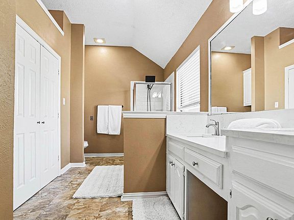 Spacious bathroom with extended vanity, large mirror, and a glass-enclosed shower, plus linen storage and tile flooring.