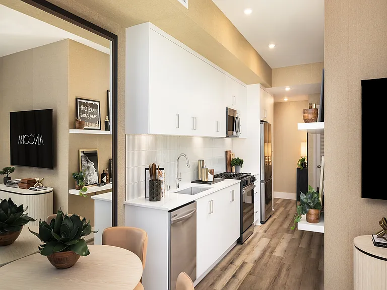 Modern kitchen with sleek white cabinetry, stainless steel appliances, and elegant wood flooring, opening to a cozy dining area.