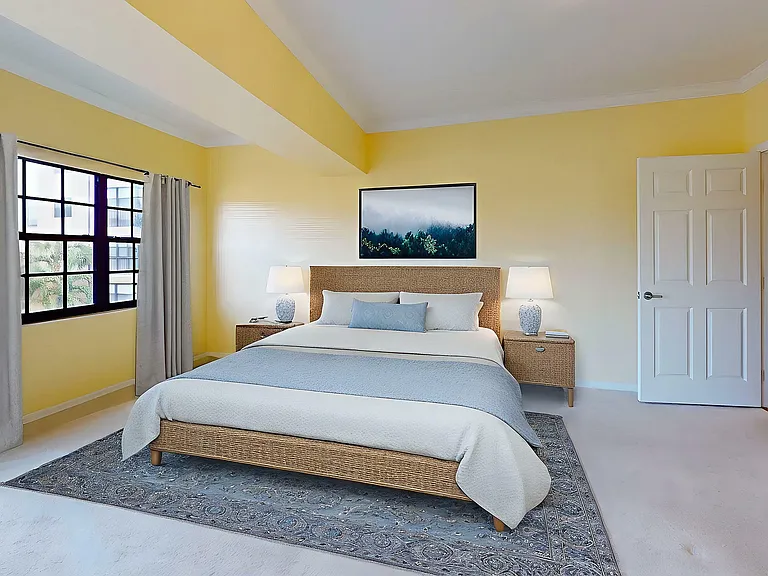Inviting bedroom with a plush bed, warm yellow walls, and a large window offering natural light and charming views.